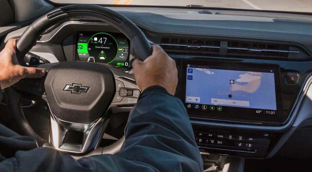 A closeup shows hands on a steering wheel driving a Chevy EV, a 2022 Chevy Bolt EUV.
