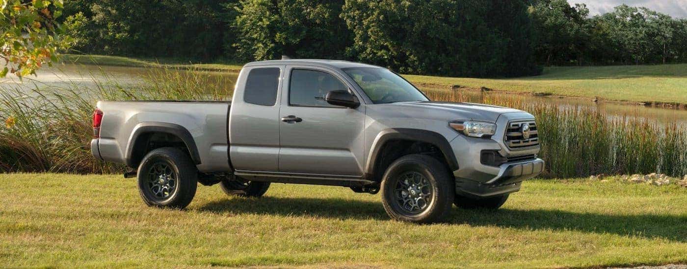 A light gray 2019 Toyota Tacoma is parked in front of a pond.