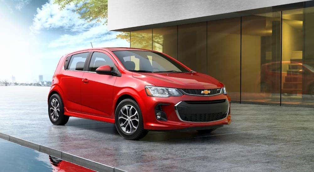 One of the best value used cars around, a red 2020 Chevy Sonic, is parked in front of a modern house.
