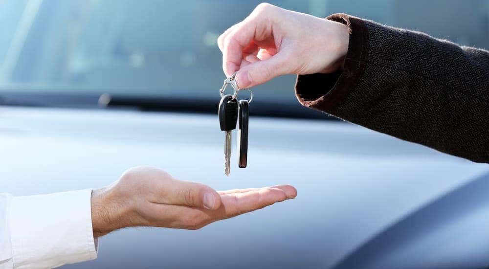 A closeup shows keys being handed from one hand to another in front of a white car.