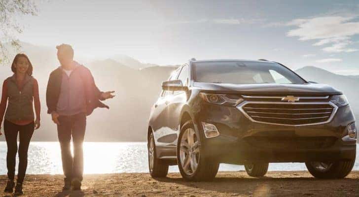A couple is walking next to a 2018 Chevy Equinox at a sunny lake.