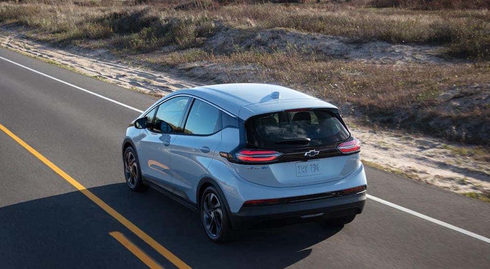 A light blue 2022 Chevy Bolt is driving down a two way road.