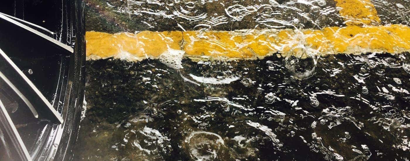 A close up shows standing water in a perking lot next to a good rain tire.