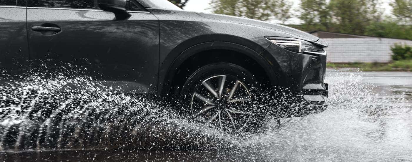 A close up shows an SUV driving on a wet highway splashing up water.