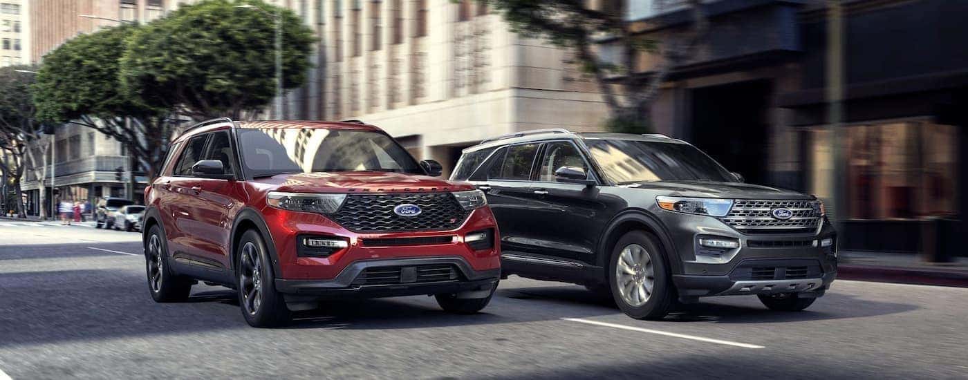 A red and a grey 2020 Ford Explorer are driving side-by-side on a city street.