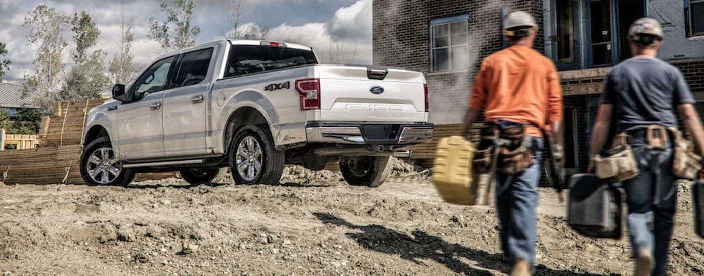 Two workers are walking toward a silver 2020 Ford F-150 at a construction site.