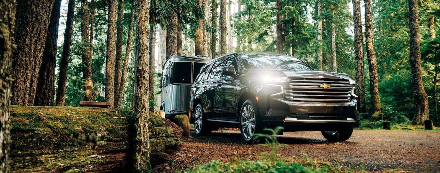 A black 2021 Chevy Tahoe High Country is shown towing an Airstream through the woods.