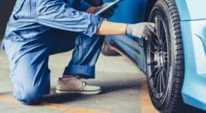 A mechanic is shown inspecting a tire on a blue car.