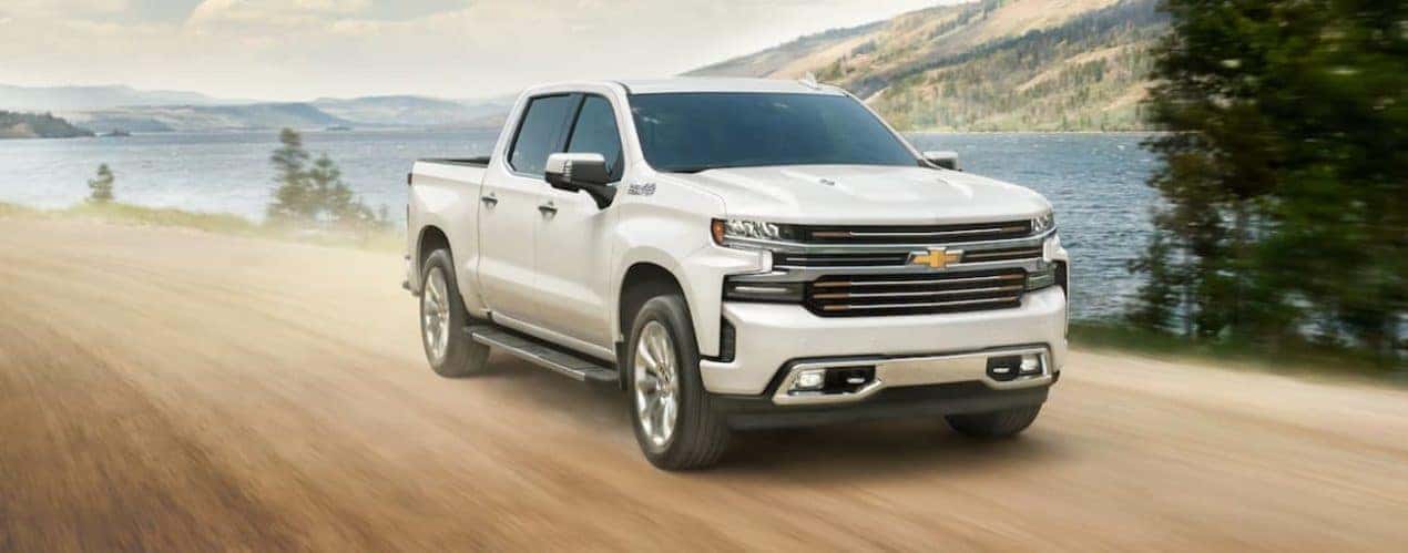 A white 2021 Chevy Silverado 1500 is driving on a dirt road past a lake.