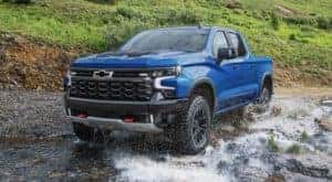 A blue 2022 Chevy Silverado 1500 ZR2 is angled left while off-roading through a puddle.