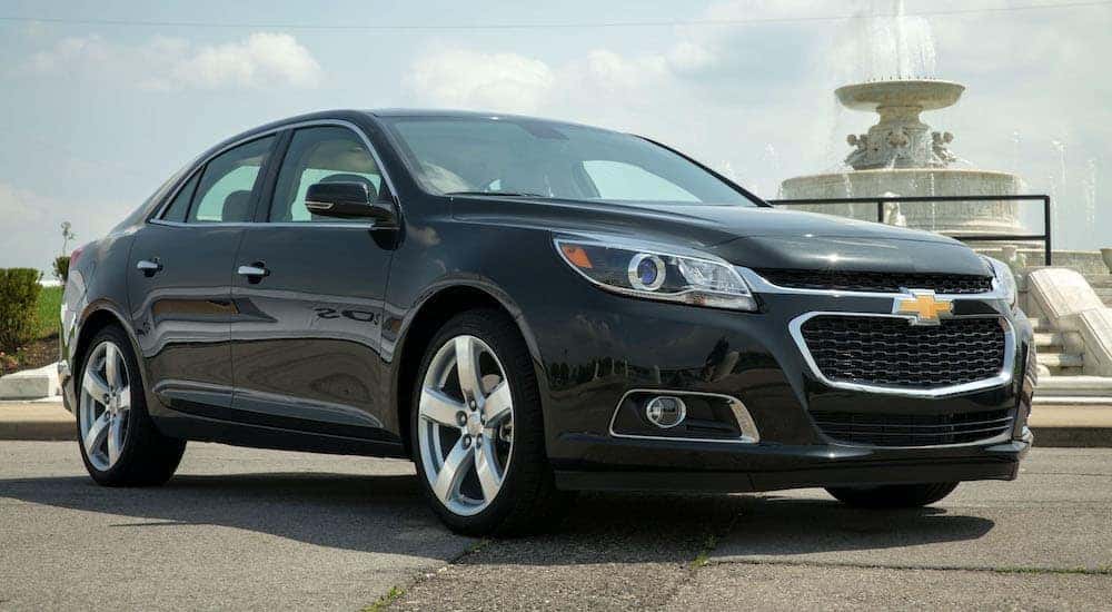A black 2014 Chevy Malibu is shown from the side parked in front of a fountain.