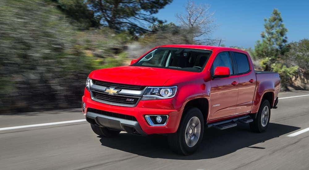 A red 2015 Chevy Colorado Z71 is shown from the front driving on an open road after leaving a Chevy dealer.
