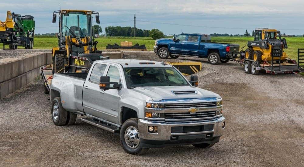A silver 2018 Chevy Silverado 2500HD is shown towing heavy machinery.