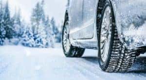 The close up shows a car driving in the snow after heading to a winter tire dealer.