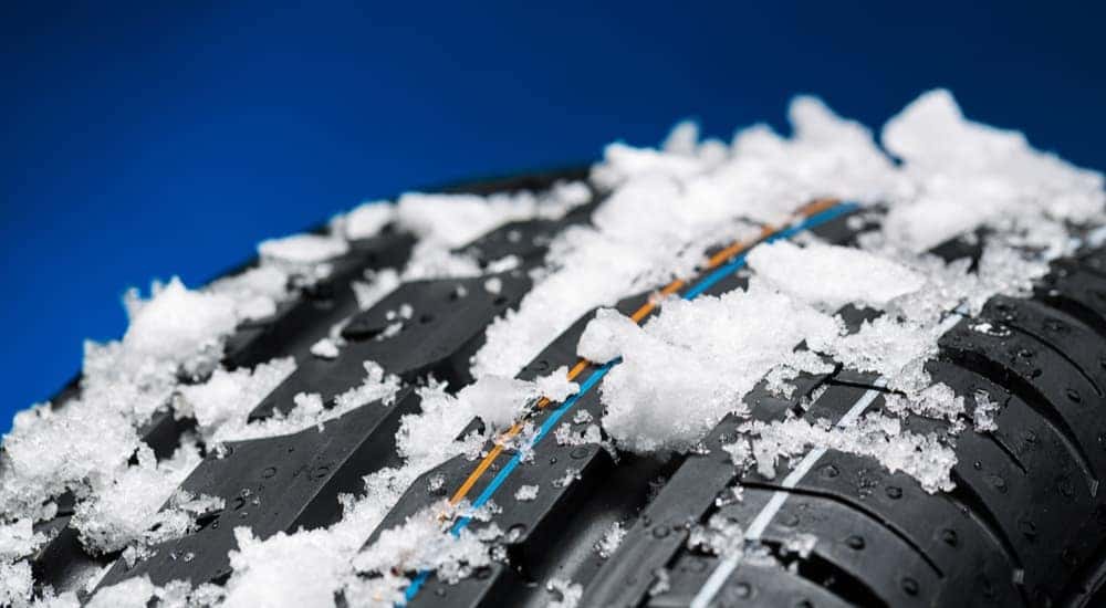 A close up shows the treads of winter tires covered in snow.