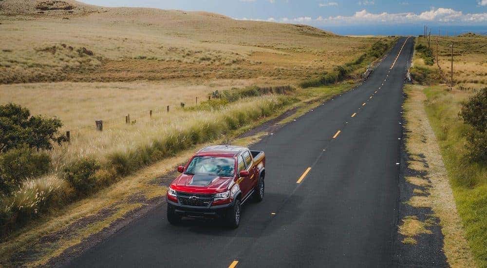 A red 2021 Chevy Colorado ZR2 is shown driving on a road past a field.