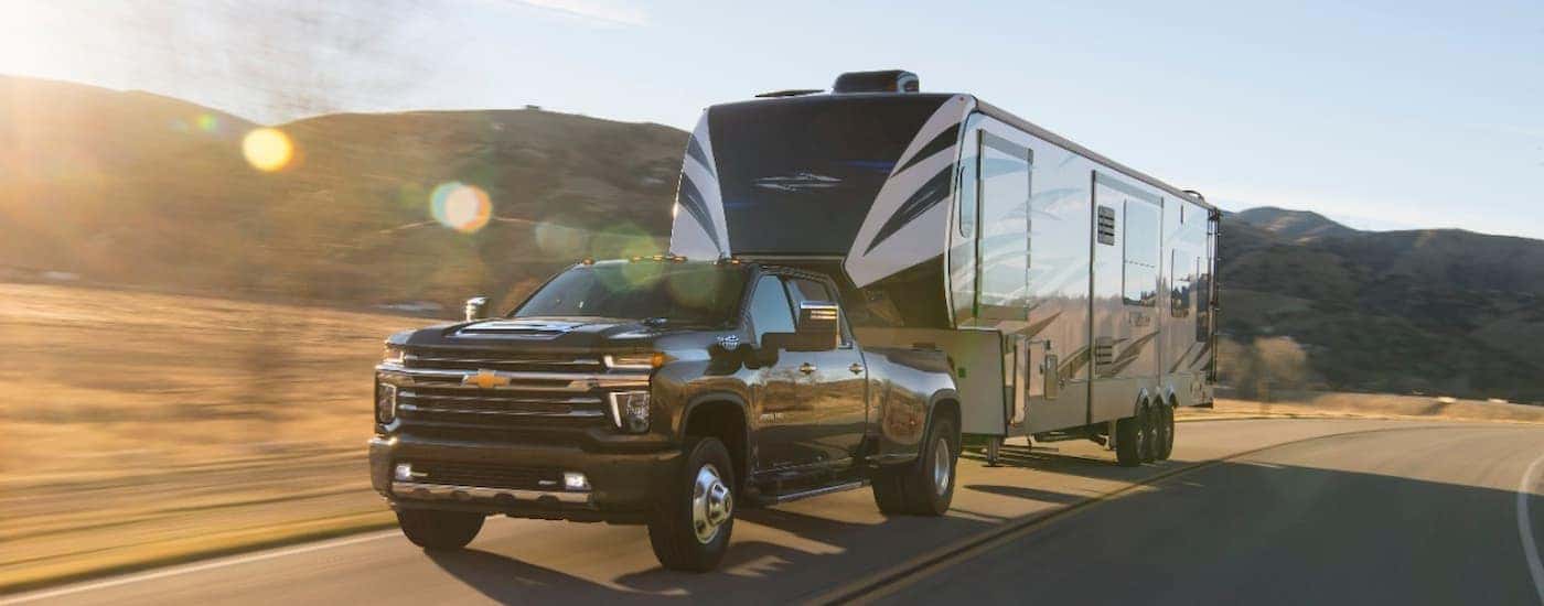 A black 2020 Chevy Silverado 3500HD DRW is shown towing a camping trailer on an open highway.