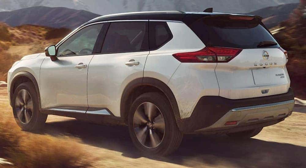 A white 2021 Nissan Rogue is shown from the rear driving on a remote dirt trail.