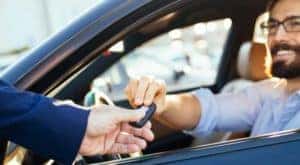 A man is shown exchanging a key with a car salesman.