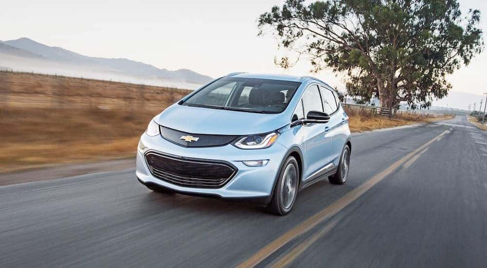 A blue 2017 Chevy Bolt EV is shown from the front at an angle while it drives down the road.
