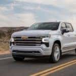 A white 2022 Silverado 1500 High Country is shown from the front at an angle while driving down the road after the owner searched 'used trucks for sale'.