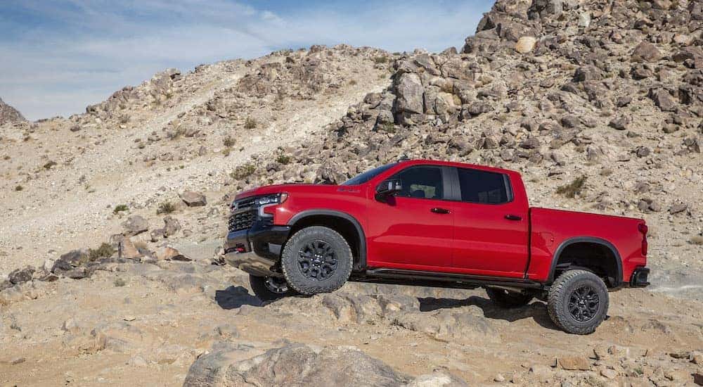 A red 2022 Chevy Silverado ZR2 is shown from the side while it crawls over rocks.