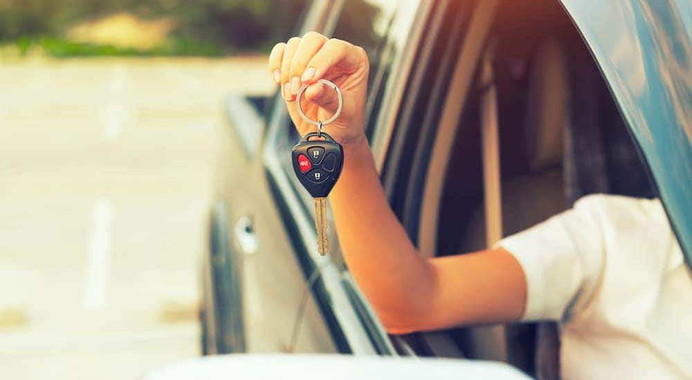 A person is shown holding a car key out the drivers side window after searching 'Used Cars Cincinnati Ohio.'
