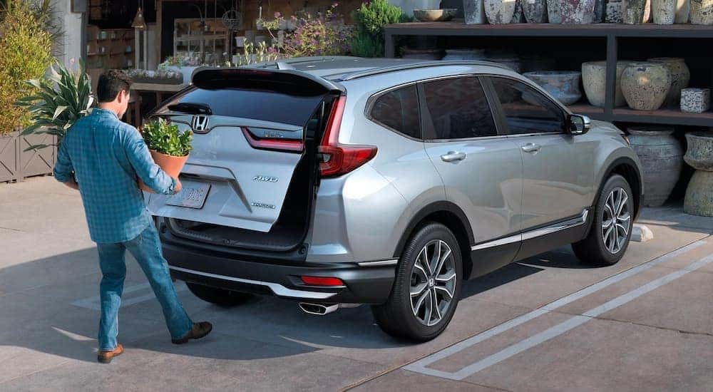 A man is shown opening the rear liftgate on a silver 2022 Honda CR-V Touring outside of a flower shop.