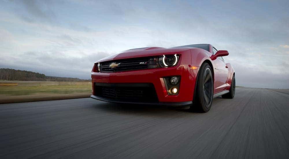 A red 2013 Chevy Camaro ZL1 is shown from a low angle driving on an open road.