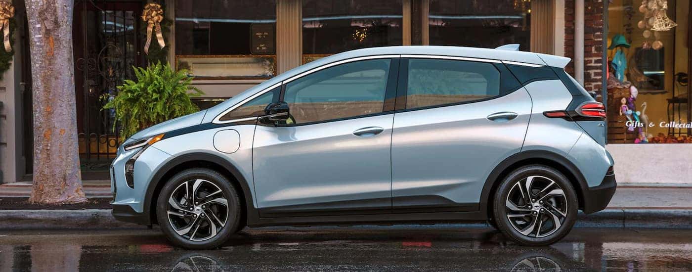 A blue 2022 Chevy Bolt EV is shown from the side parked in front of a city building.