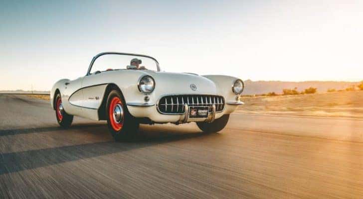 A white 1957 Chevy Corvette is shown driving on a highway.