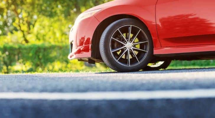 A close up shows the wheel and tire on a red car.