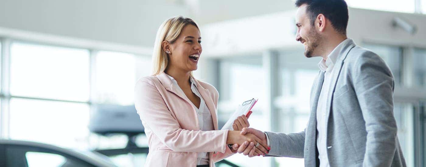 A salesperson is shown shaking hands with a customer after searching 'value my car.'