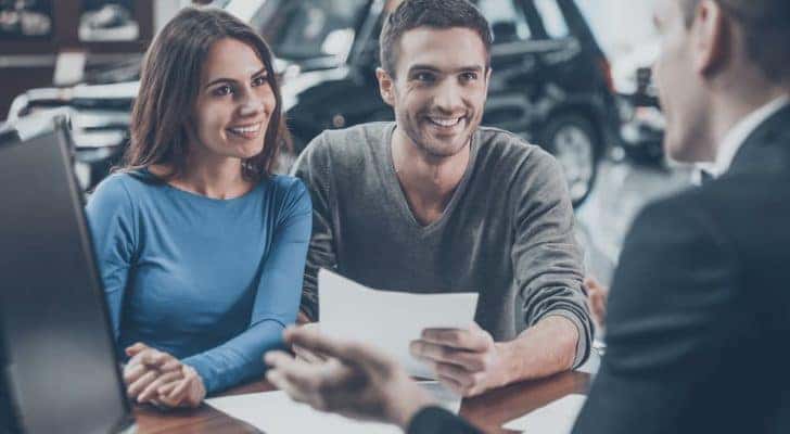 A couple is shown talking to a salesperson about valuing their car.