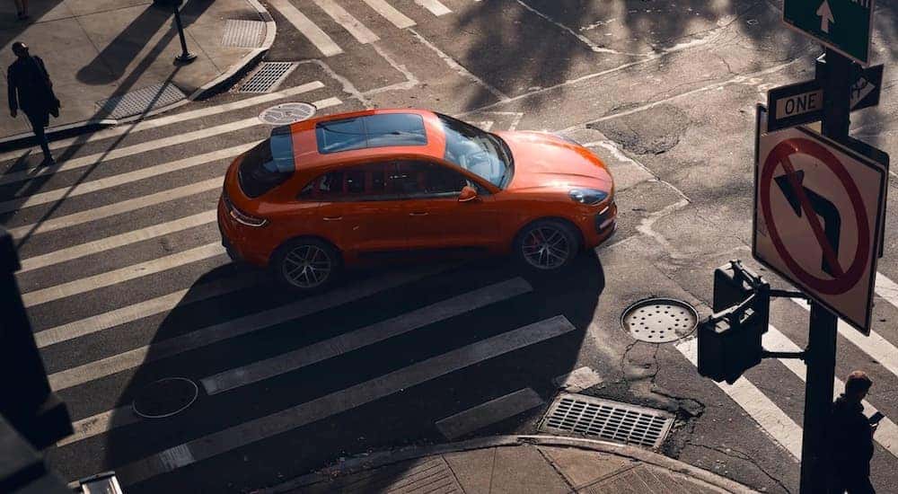 An orange 2020 Porsche Macan is shown from a high angle while crossing an intersection.