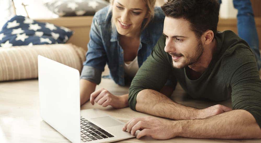A couple is shown searching, 'How Does Buy Here Pay Here Work', on their laptop.