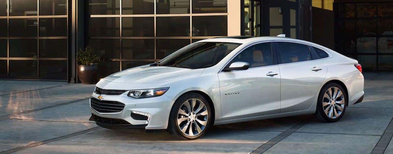 A white 2017 Chevy Malibu is shown parked outside of a driveway.