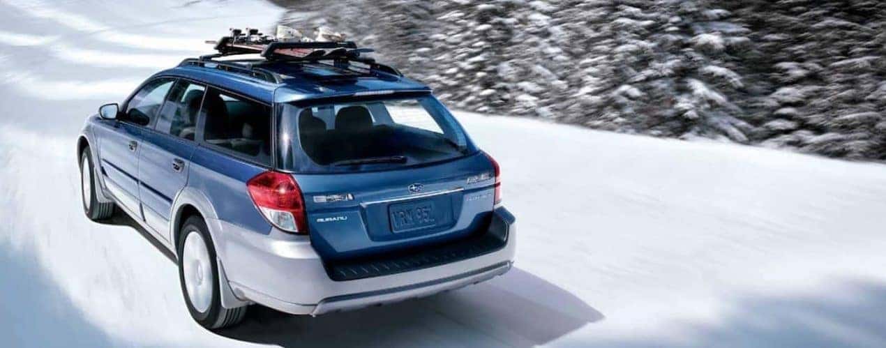 A blue 2009 used Subaru Outback is shown driving on a snow-covered road.