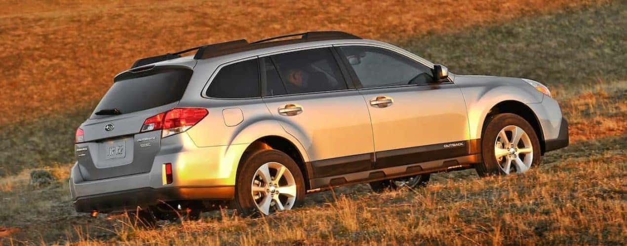 A silver 2014 Subaru Outback is shown from a rear angle driving through a field.