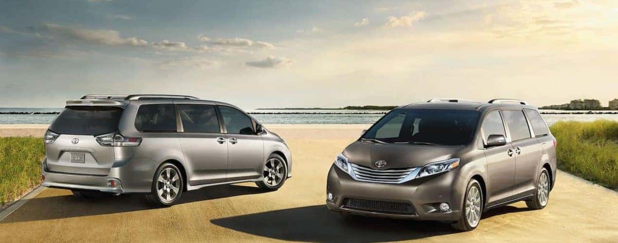 A grey and a silver 2015 Toyota Sienna are shown parked on a sandy road.