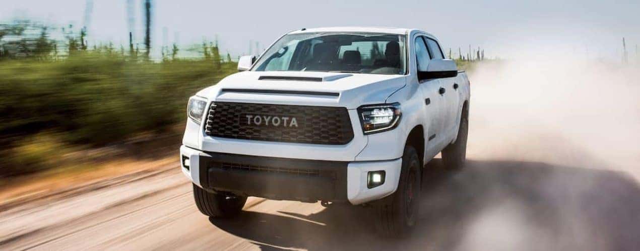 A white 2019 Toyota Tundra is shown from the front driving on a dusty road.