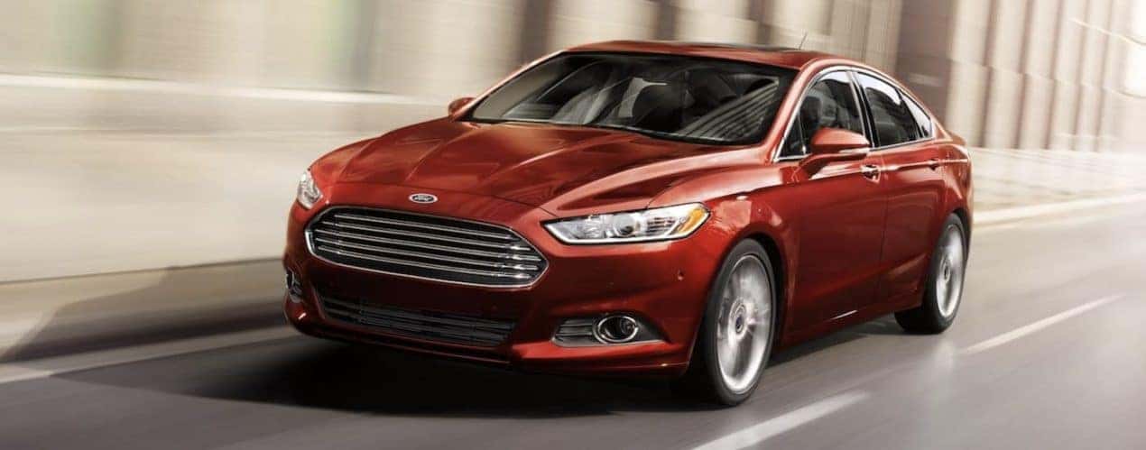 A red 2014 Ford Fusion is shown driving on a two lane highway.