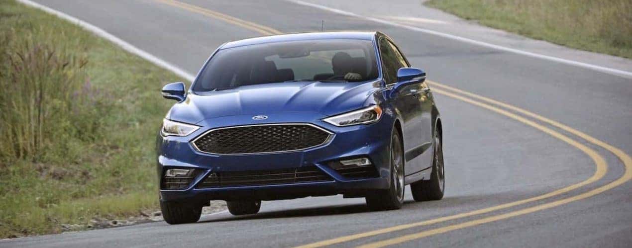A blue 2017 Ford Fusion is shown driving on an open road.