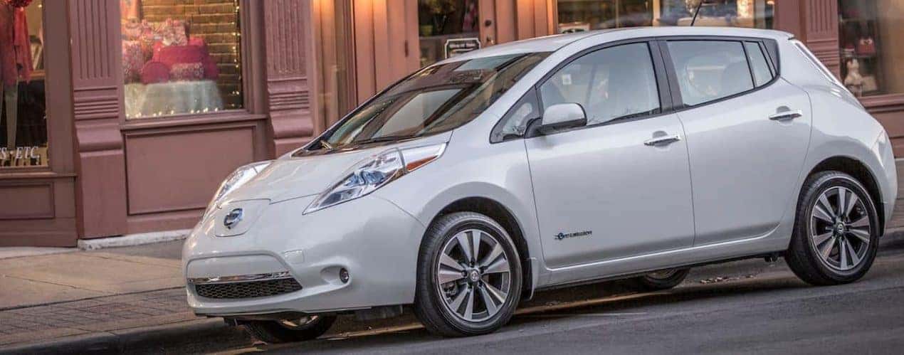 A white 2015 Nissan Leaf is shown from the side on a city street.