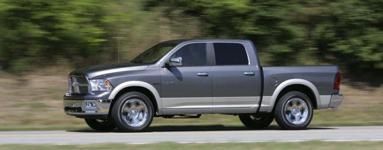 A grey 2011 Ram 1500 is shown from the side driving on a tree-lined road.