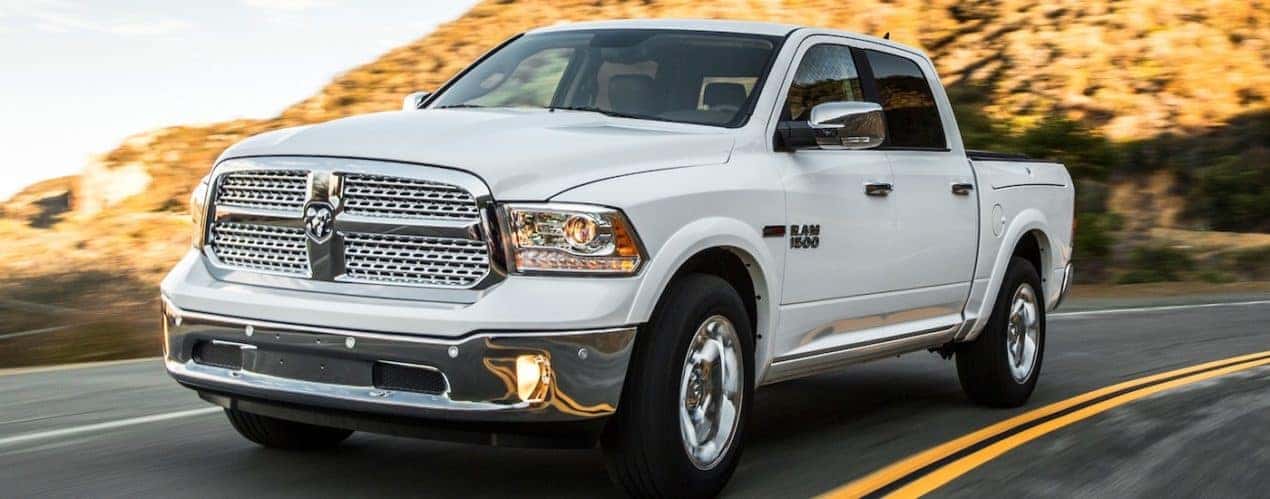 A white 2014 Ram 1500 is shown driving on an open road.
