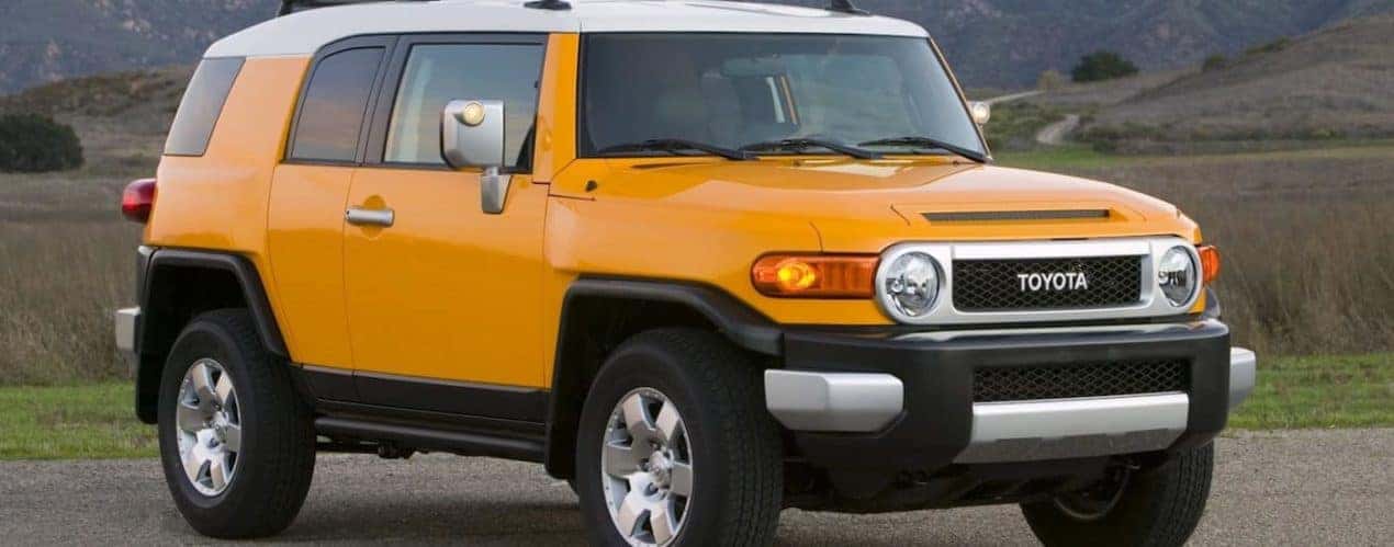A yellow used 2009 Toyota FJ Cruiser is shown parked near a grassy field.
