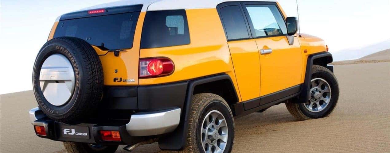 A yellow 2013 Toyota FJ Cruiser is shown from the rear parked in a desert.