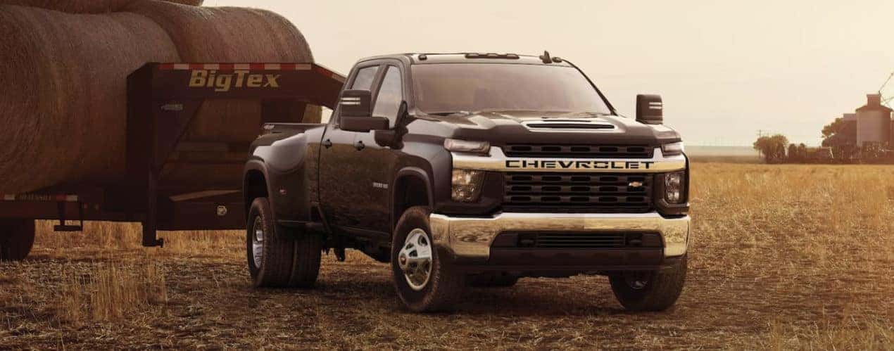 A black 2023 Chevy Silverado 3500 HD is shown parked in a field towing a hay trailer.
