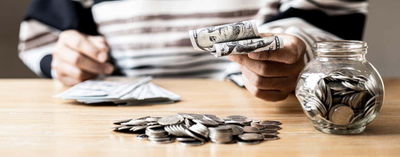 A person is shown with cash and coins on a table.